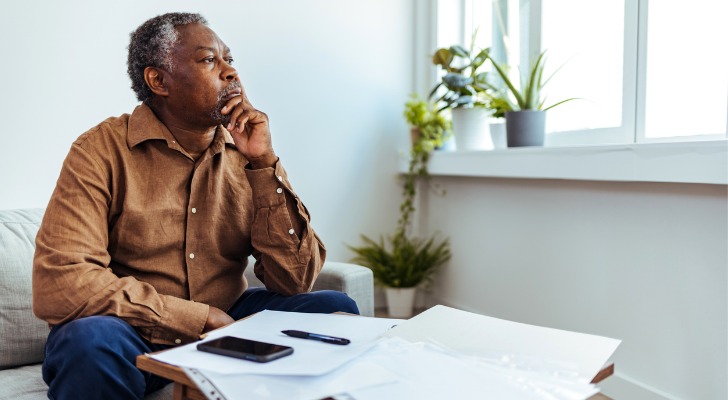 A man in his 60s appears to be in deep thought while doing some paperwork. 