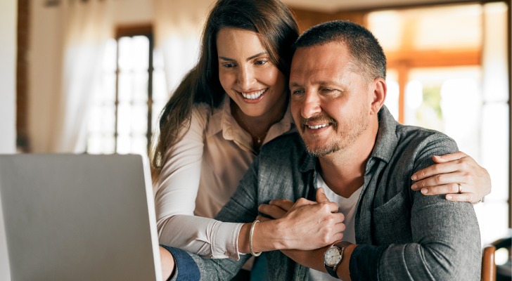 A woman embraces her husband as they look at a computer screen together. 